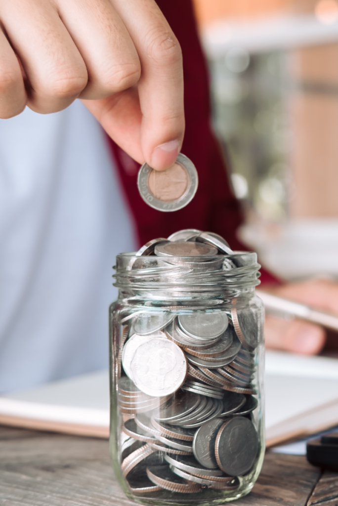 Une personne économisant des pièces dans un pot sur un bureau pour économiser.